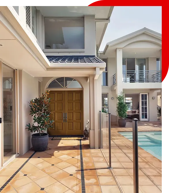 Modern house entrance with double wooden doors, potted plants, tiled floor, and a glass fence next to a swimming pool.