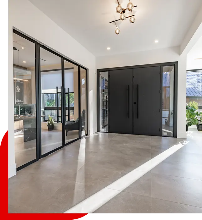 Modern entryway with large black double front doors, glass interior partition with black frames, and beige tile flooring illuminated by natural light.