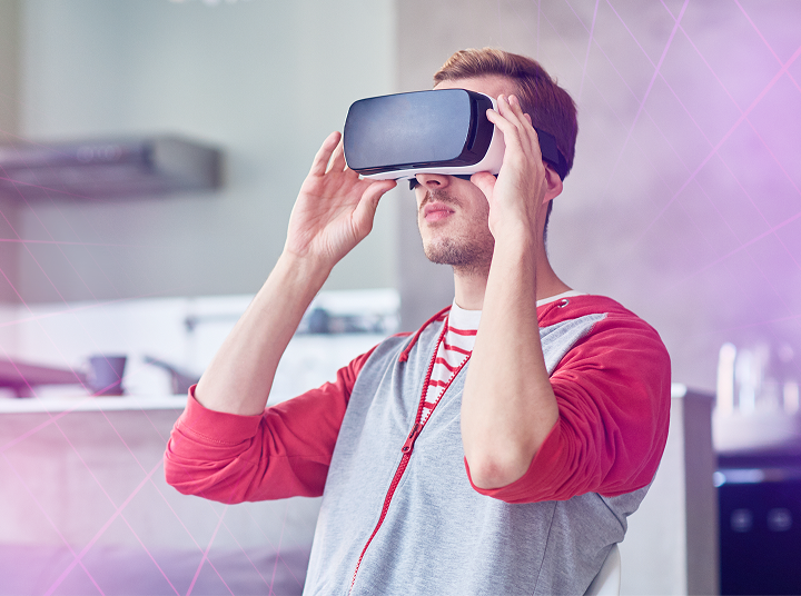 Young man wearing a red and gray hoodie uses a virtual reality headset indoors.