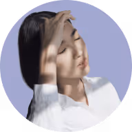 Young woman with eyes closed shielding her face from sunlight with her hand.