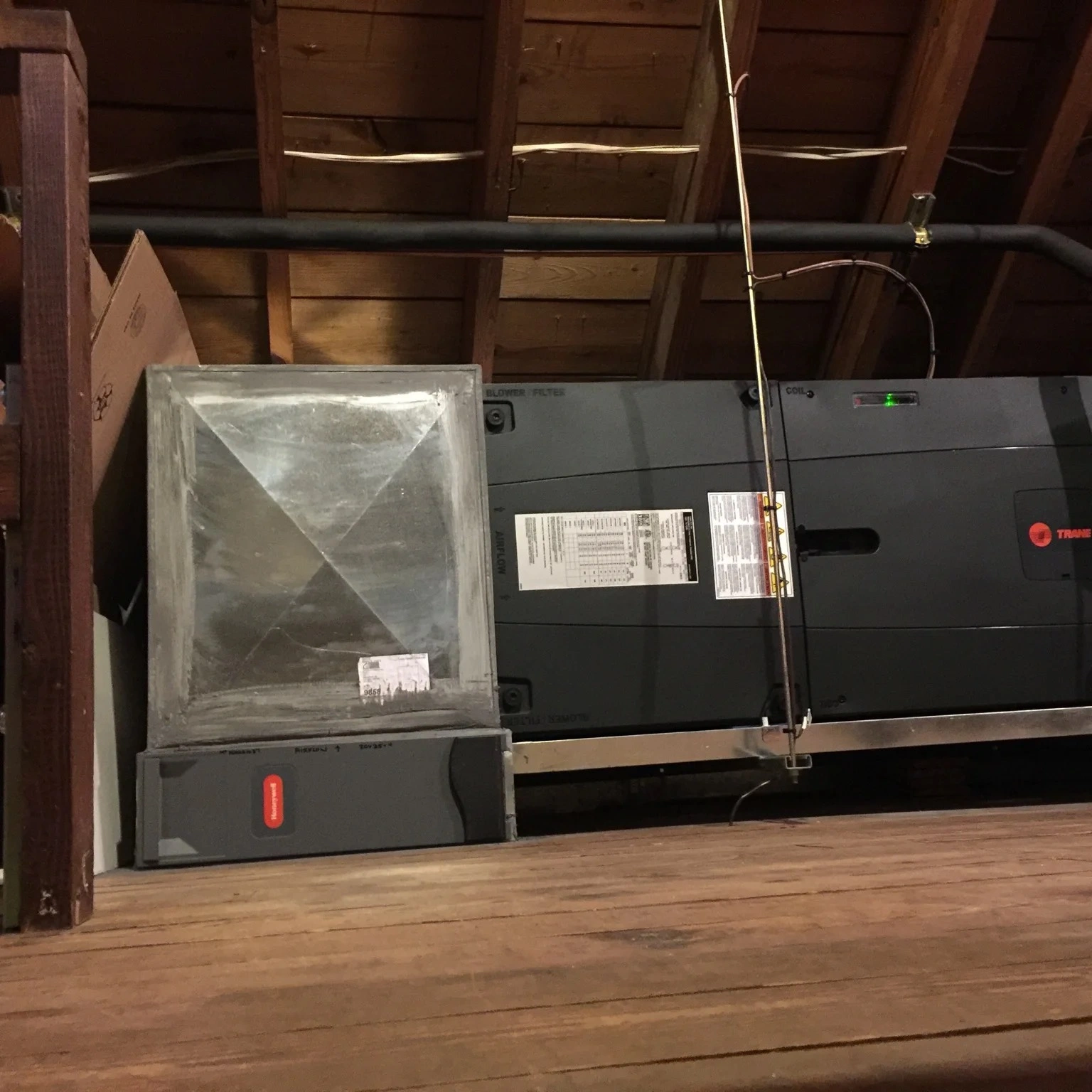An HVAC unit in a wooden attic space, featuring a large, rectangular metal component and visible ventilation ducts conveying a functional tone.