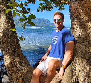 Steve Mugford sitting on a tree at a beach