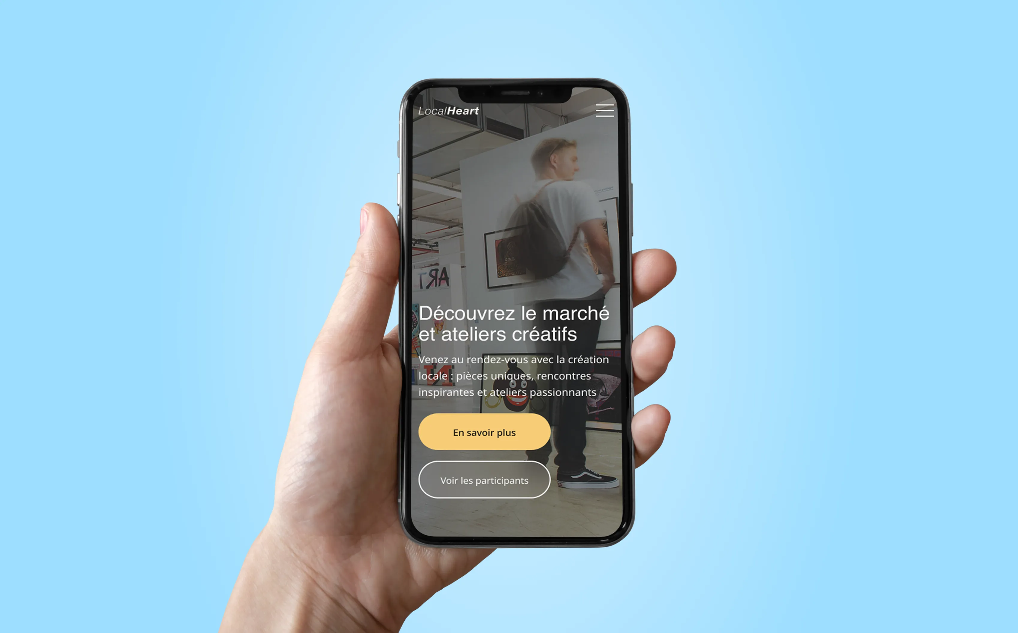 Hand holding smartphone displaying a webpage in French about a creative market and workshops with buttons for learning more and seeing participants.