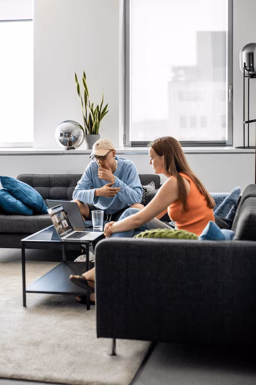 Two people sitting in a Povio office lounge area looking at a laptop on a black coffee table.