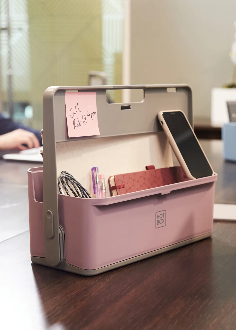 Pink and grey Hotbox organiser holding a smartphone, notebook, pens, and a charging cable.