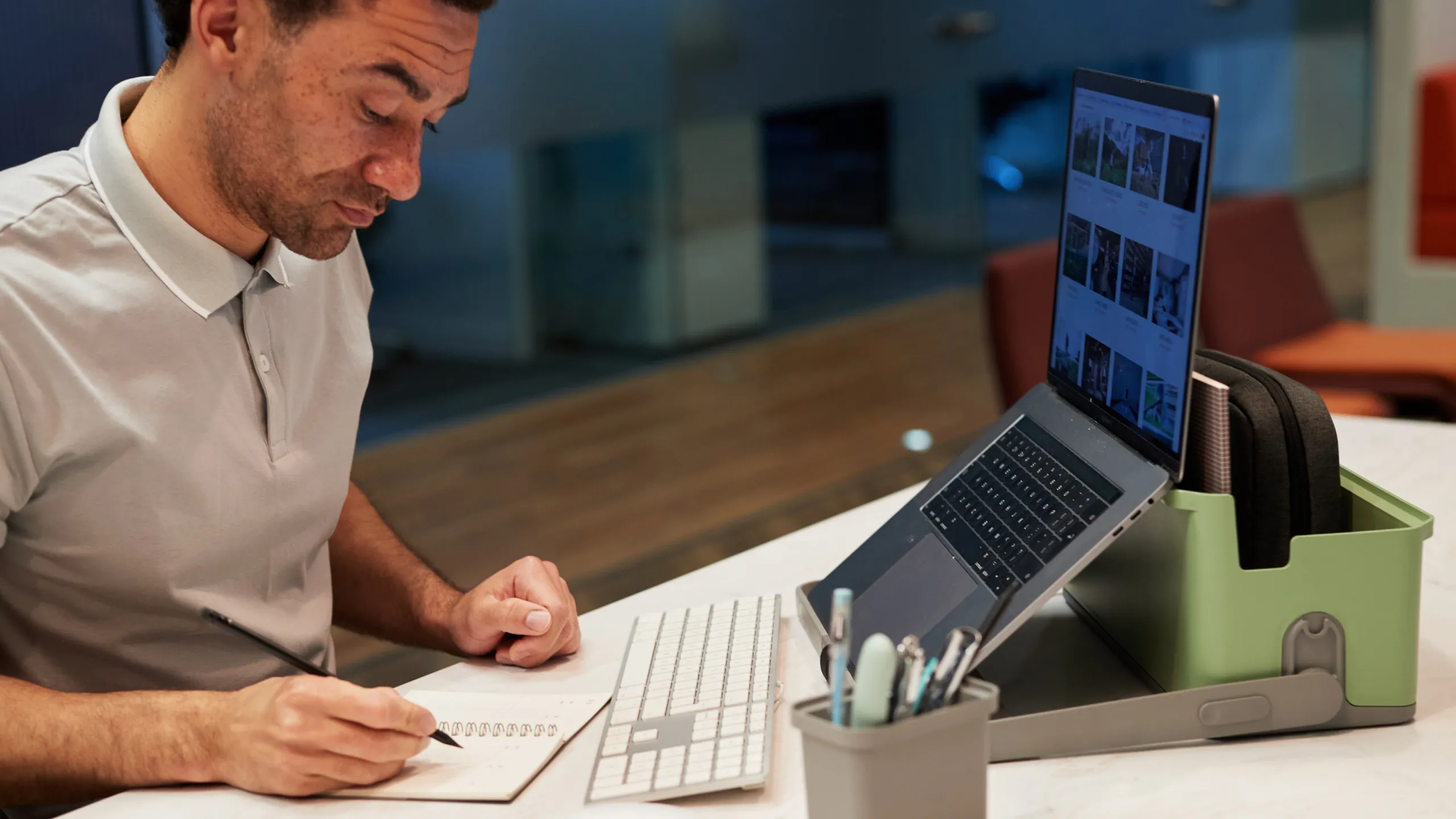Man writing in a notebook at a desk with a keyboard and laptop on a green Hotbox 4 stand.