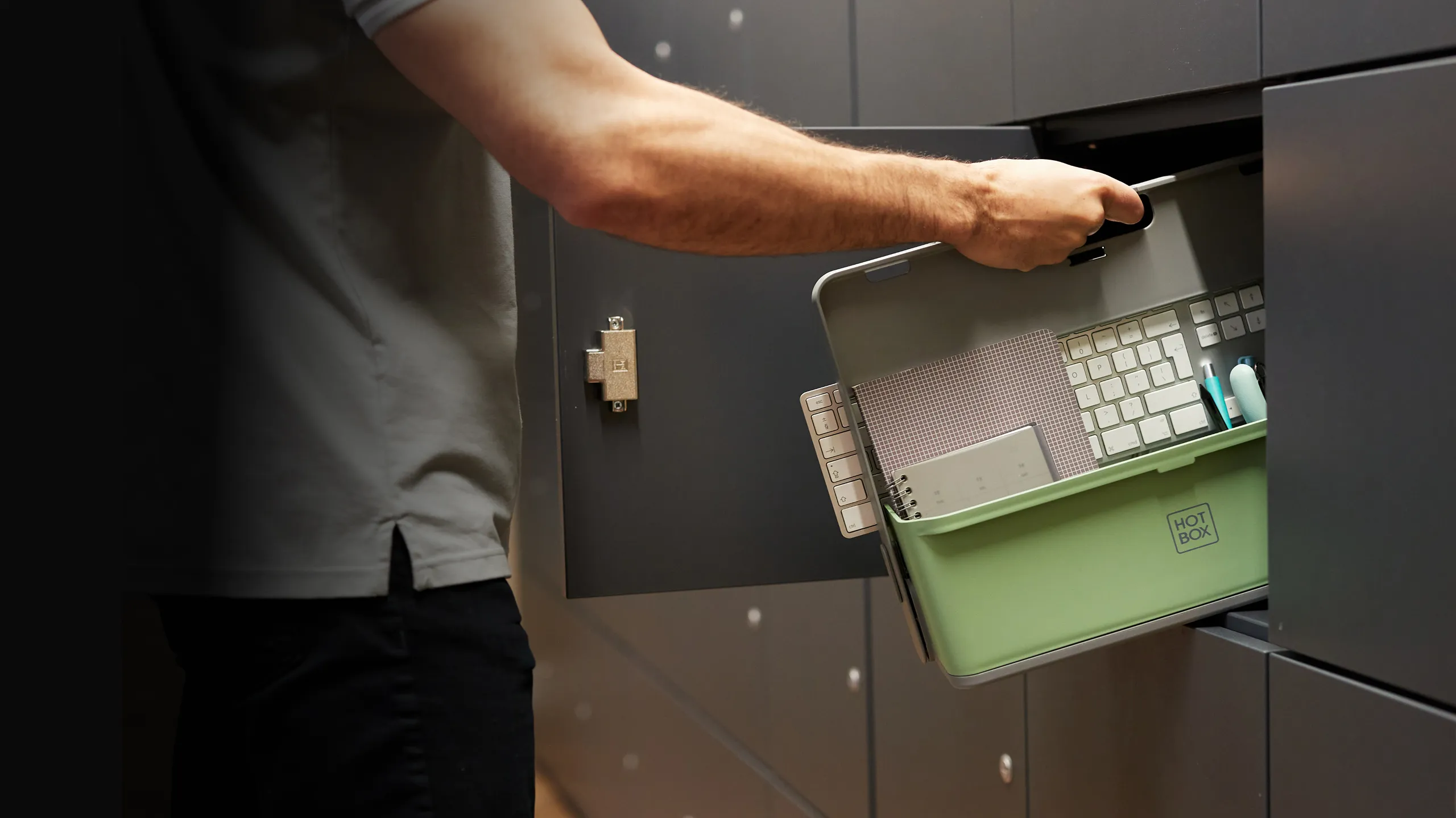 Person placing a green Hotbox container filled with keyboard, notebook, and pens into a grey locker.
