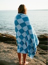 Person wrapped in blue and white checkered blanket standing on rocks by the sea.