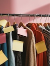 Clothes hanging on a rack with pink, yellow, and cream price tags against a pink background.