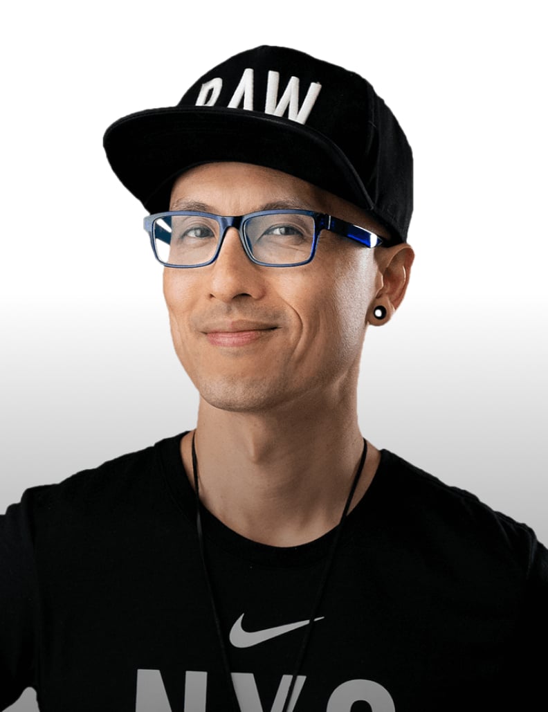 Smiling man wearing blue glasses, black cap with RAW, black Nike shirt, and black ear plugs on white background.
