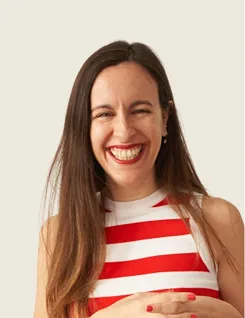 Smiling woman with long brown hair in a red and white striped sleeveless top against a neutral background.