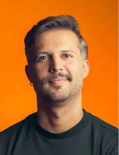 Man with short hair and mustache smiling against an orange background wearing a black shirt.