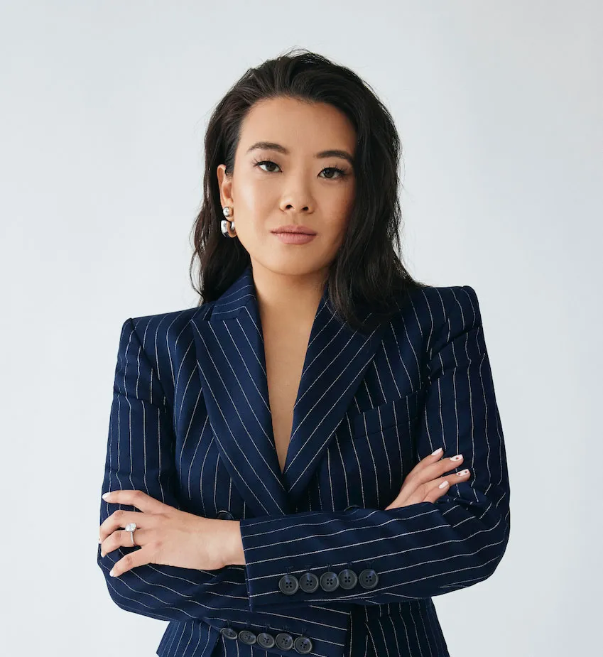 Confident woman with dark hair in a navy pinstripe blazer, arms crossed, against a light background.