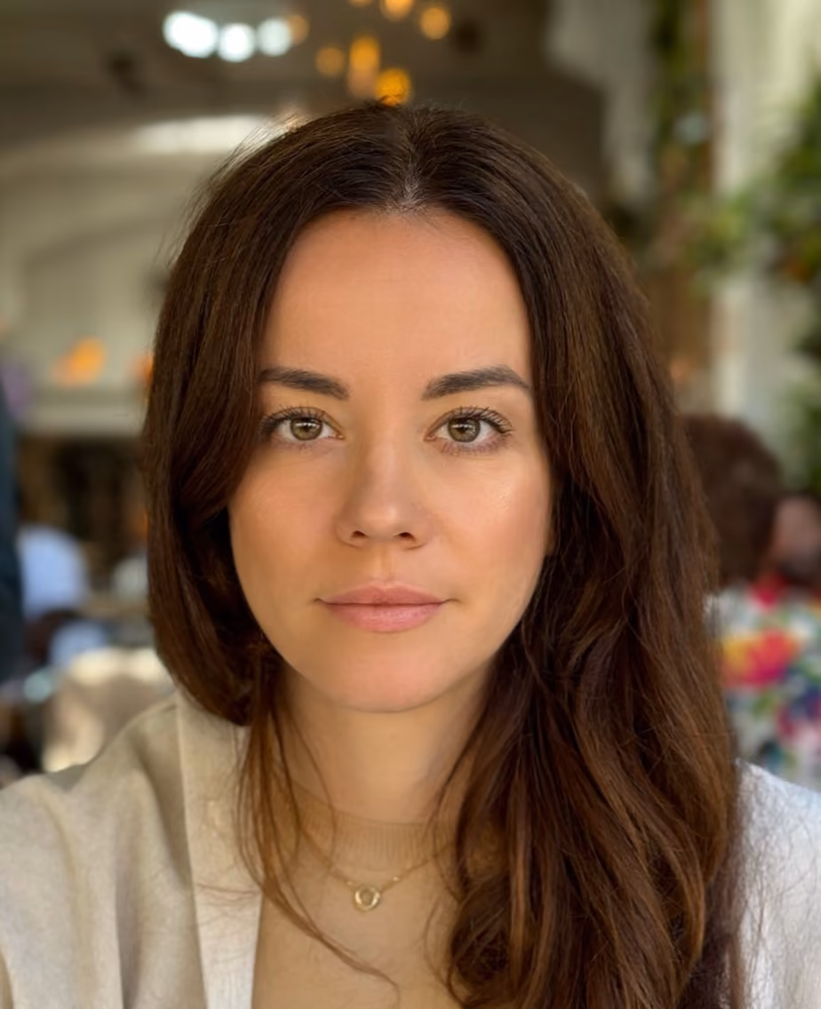 Close-up of a woman with long brown hair, light makeup, and a necklace with a heart pendant.