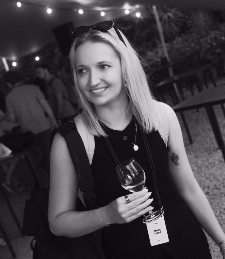 Smiling woman with sunglasses on her head holding a wine glass at an outdoor event.