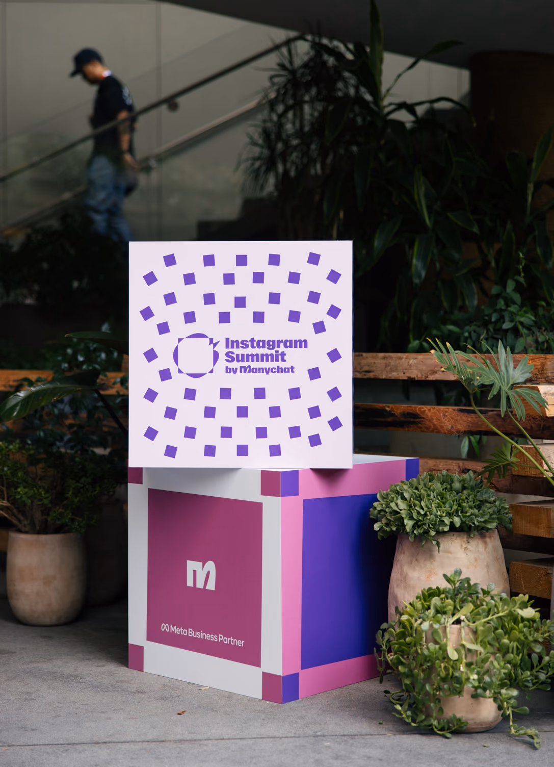 Decorative cube with Instagram Summit by Manychat and Meta Business Partner logos near potted plants.