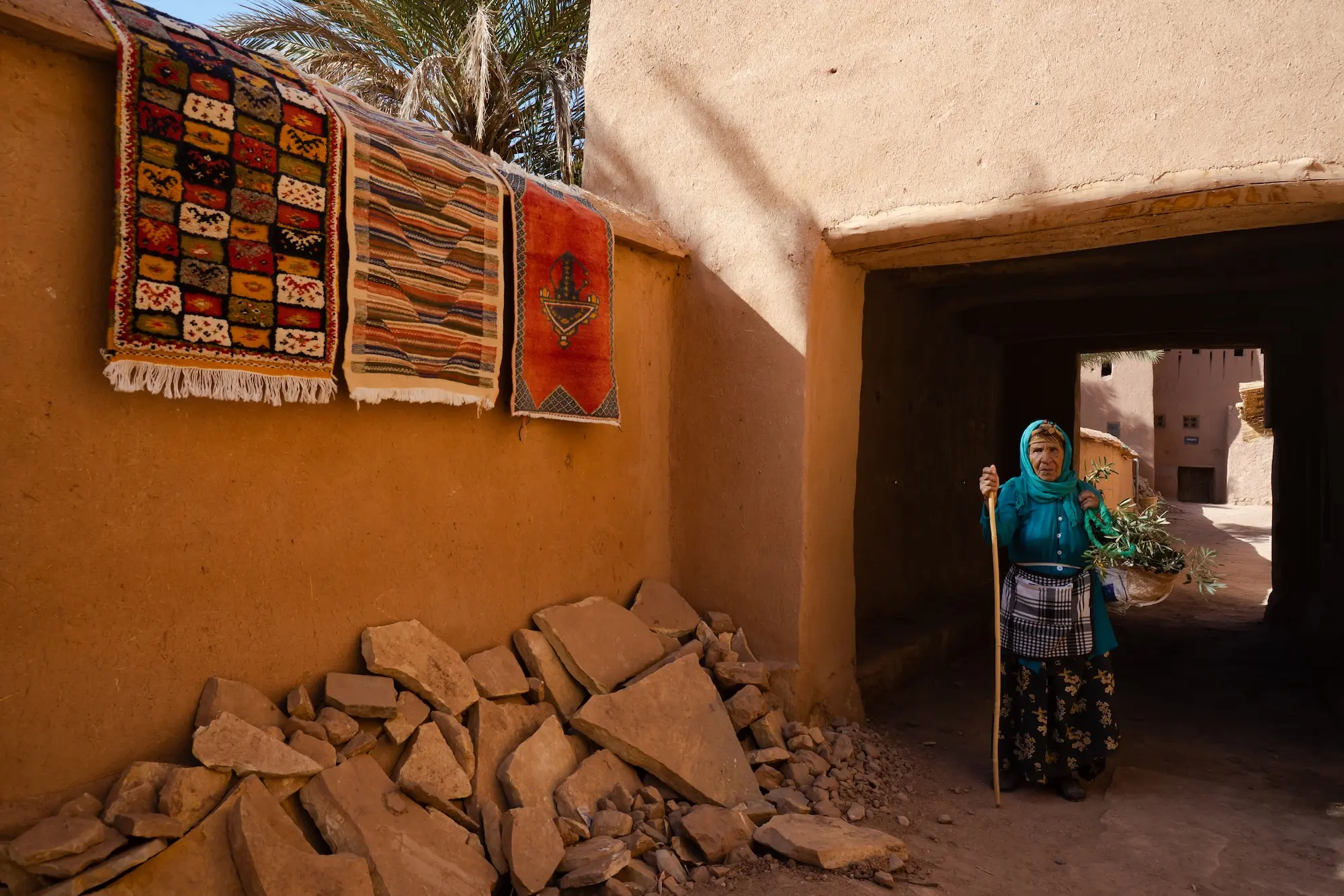 Traditional woman standing next to local rugs in Ait Ben Haddou