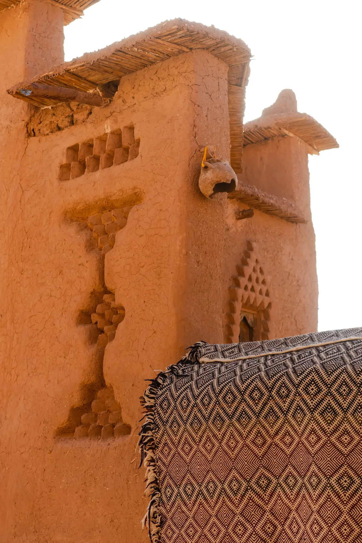 A Moroccan rug hanging on a mudbrick wall with decorative motifs in Ait Ben Haddou