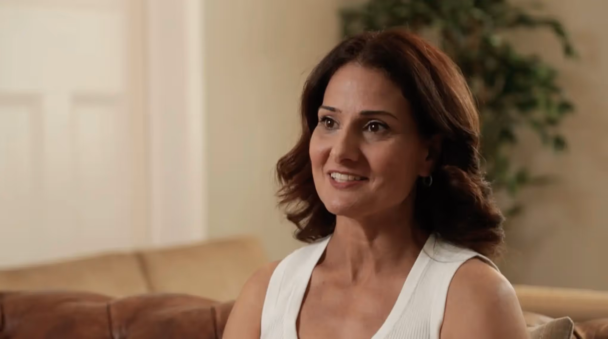 Smiling woman with shoulder-length brown hair sitting on a couch in a living room.
