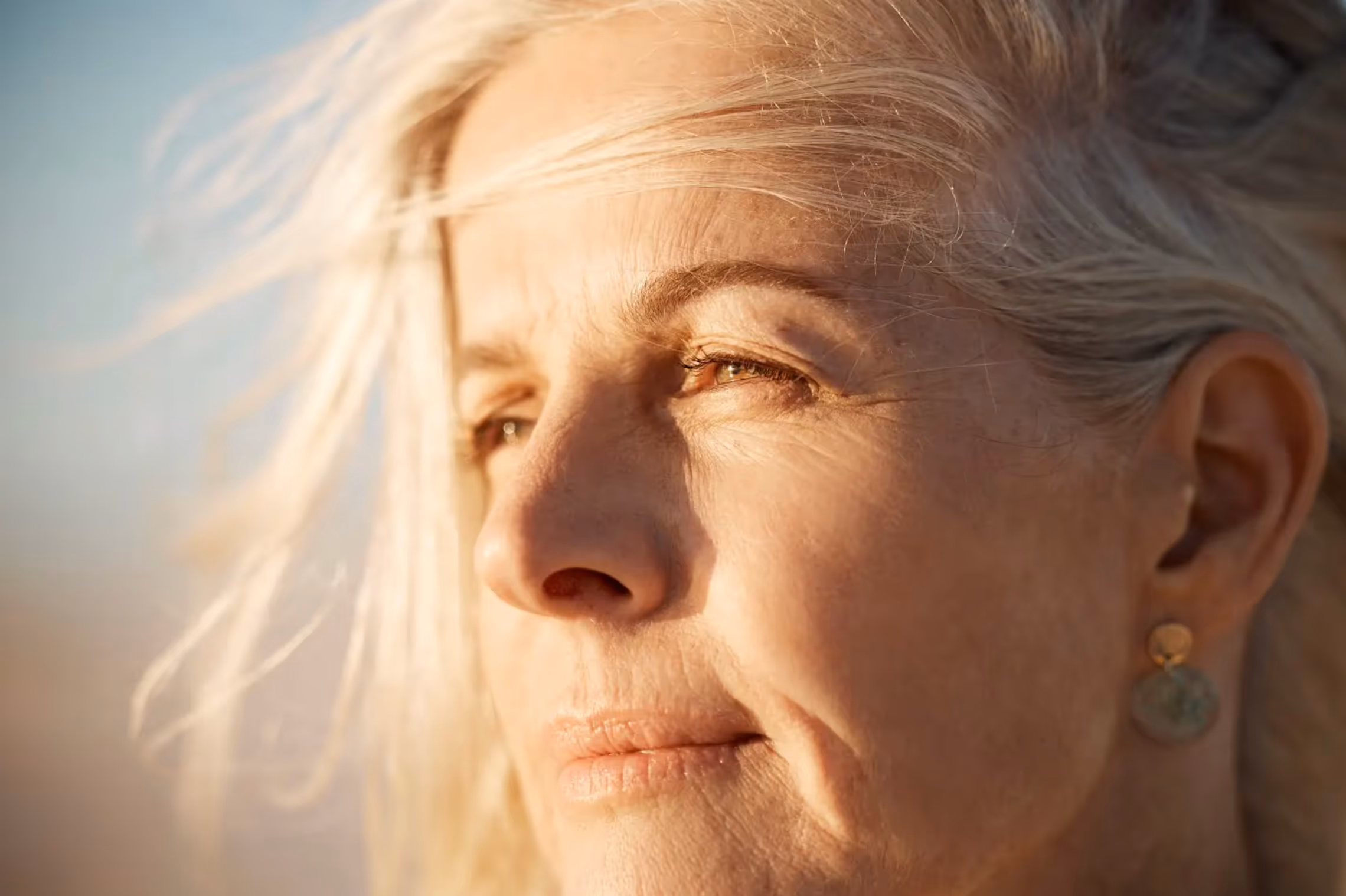 Close-up of a mature woman with blonde hair looking thoughtfully into the sunlight.