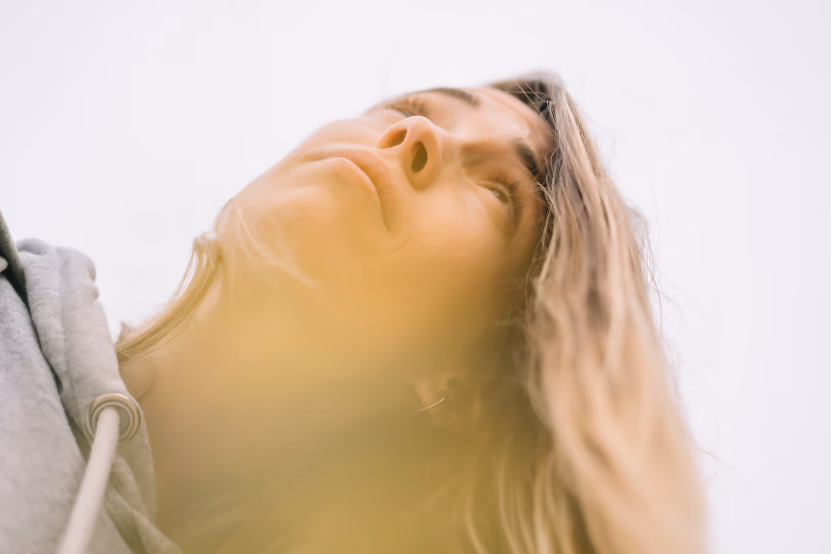 Close-up low-angle view of a woman with long hair looking thoughtfully into the distance against a bright sky.