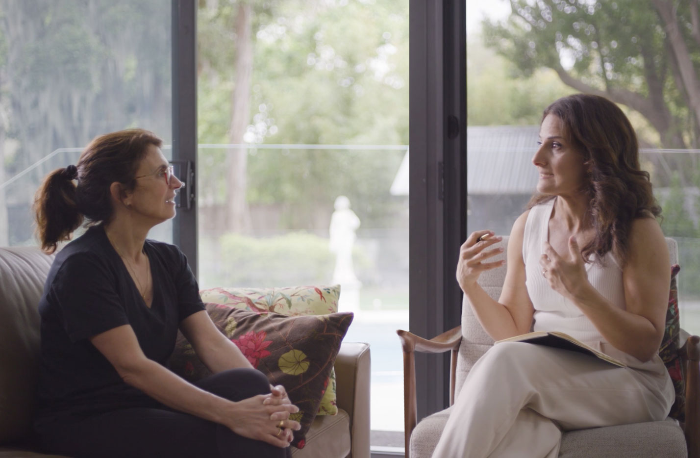 Berta Azzi and a patient sitting indoors facing each other and having a conversation, with natural light from a large window behind them.