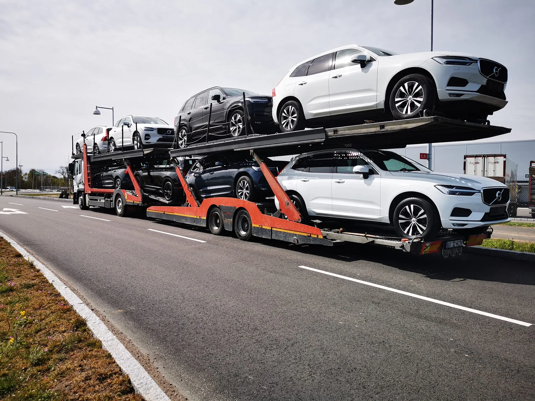 Car carrier truck loaded with multiple white and black Volvo SUV cars parked on the road.