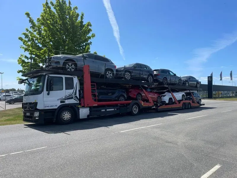 Car carrier truck loaded with multiple cars parked on the side of the road under a clear blue sky.