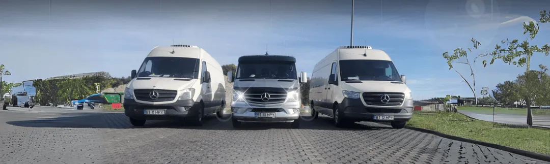 Three Mercedes-Benz delivery vans parked side by side on a paved area with a clear sky background.