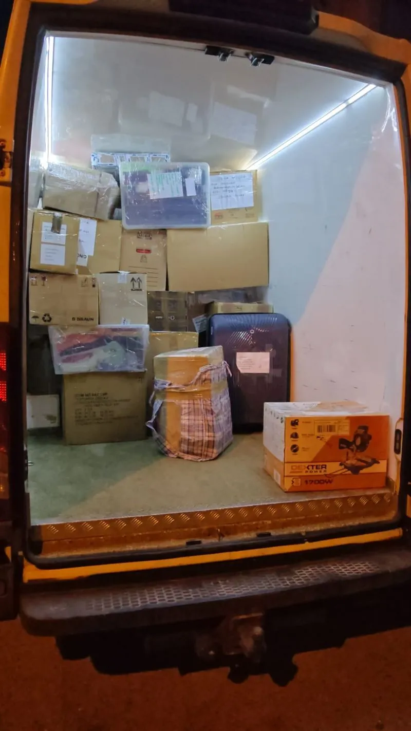 Open van back loaded with various cardboard boxes, plastic containers, and a suitcase.