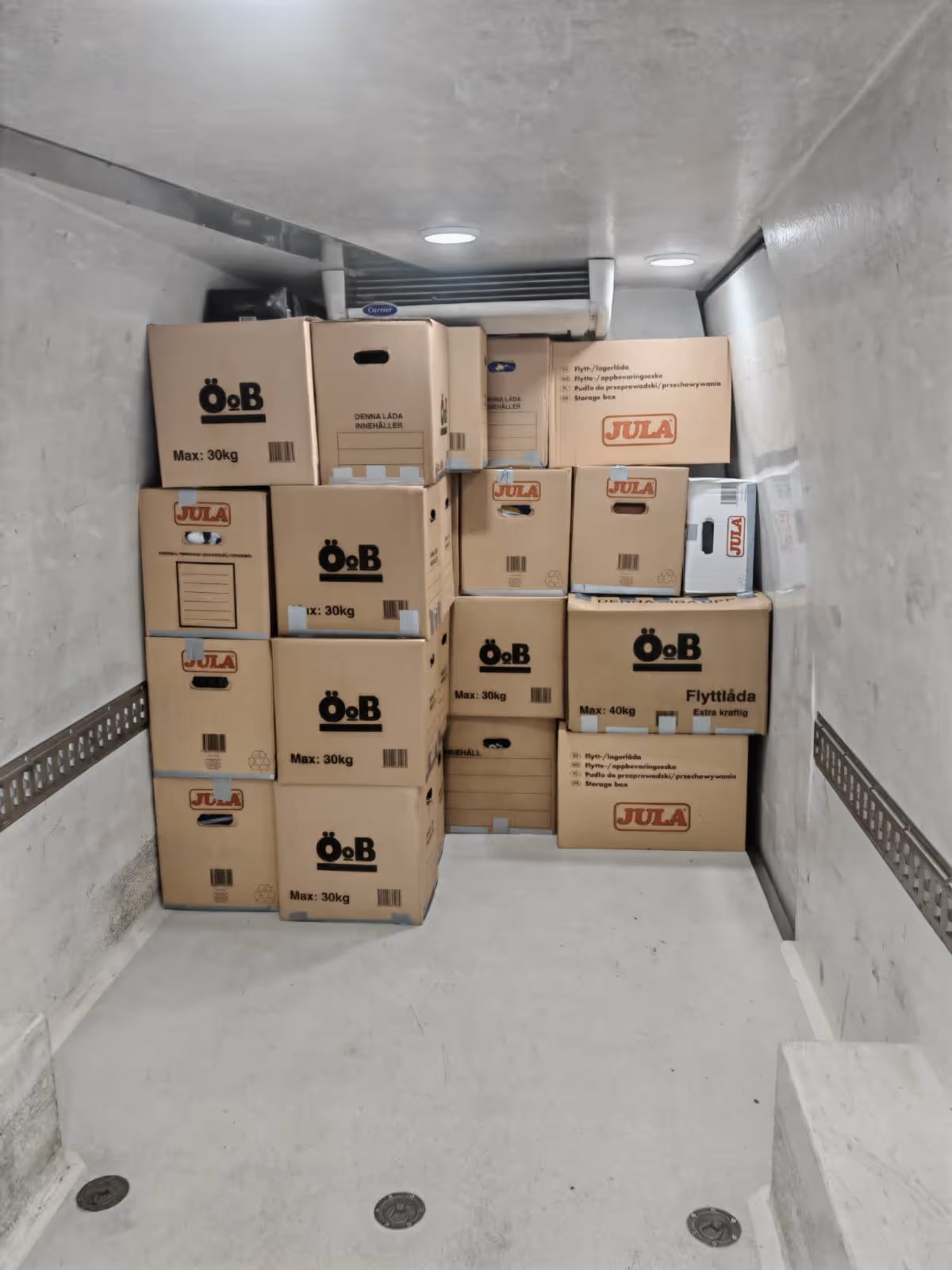 Stack of labeled cardboard moving boxes neatly arranged inside a vehicle with white walls and ceiling.