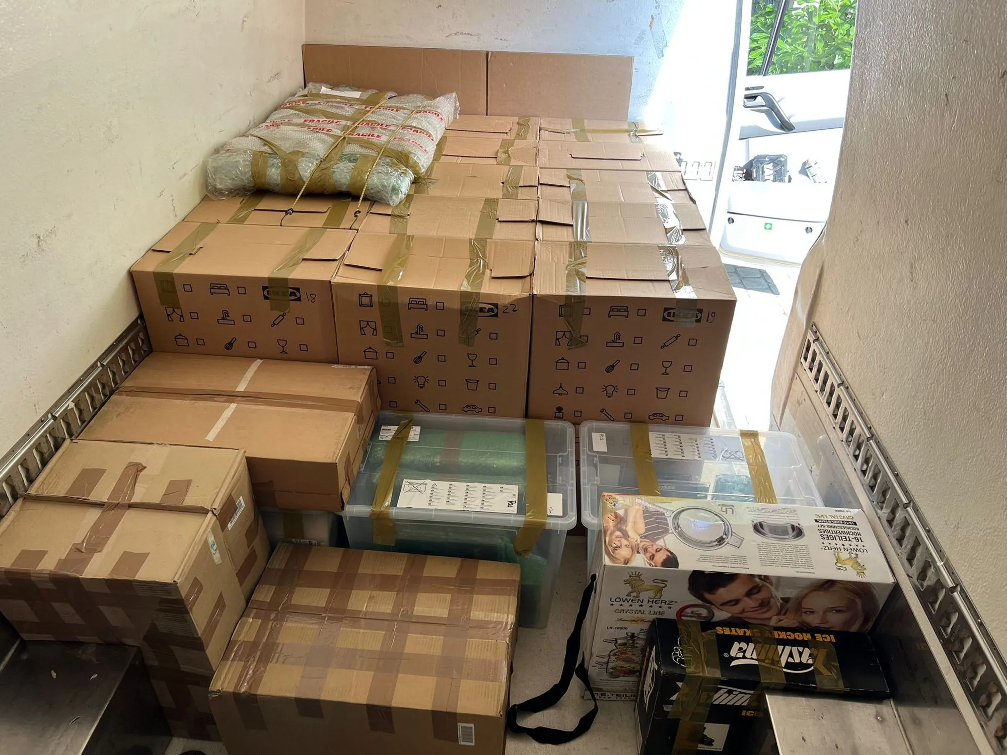 Stack of sealed cardboard boxes and plastic containers packed neatly inside a delivery van with the door open.