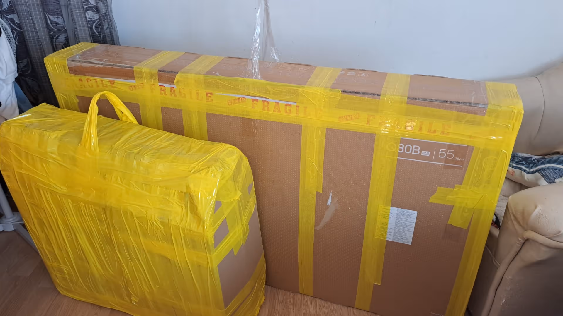 Two large cardboard packages wrapped securely with yellow tape labeled 'Fragile,' placed indoors near a couch and window.