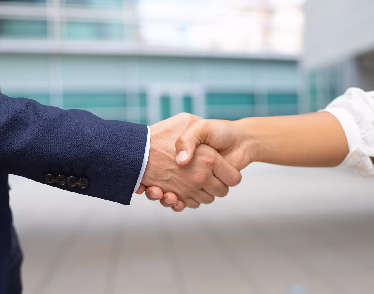 Close-up of a handshake between a person in a dark suit and a person in a white shirt in an urban setting.