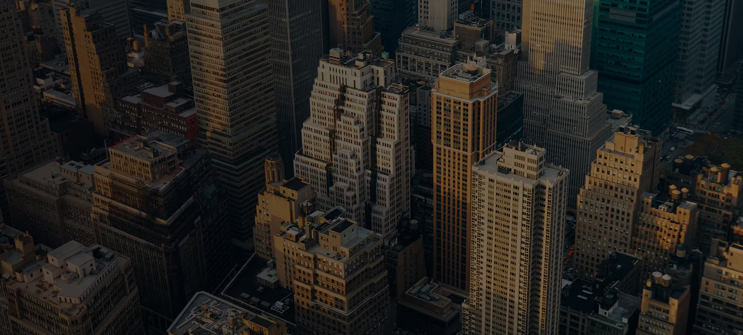 Aerial view of densely packed skyscrapers in a city during sunset with warm light casting shadows.