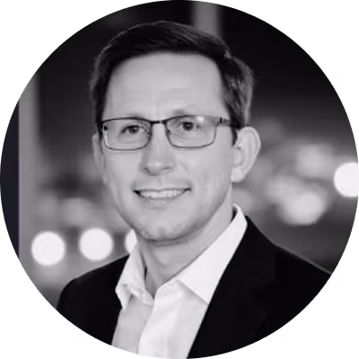 Portrait of a man wearing glasses and a suit jacket smiling against a blurred background.