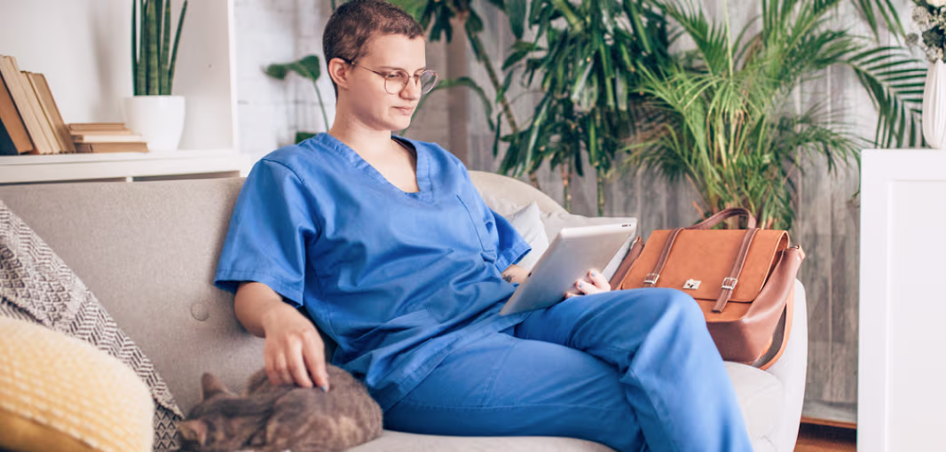 Provet professional in blue scrubs relaxing with tablet and cat at home