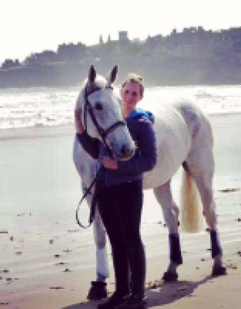 Provet white horse and rider standing together on misty beach