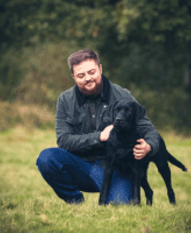 Provet veterinarian hugging a black dog in a grassy outdoor setting