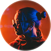 Portrait of a woman with tied-back hair and glasses, illuminated by red and blue light.
