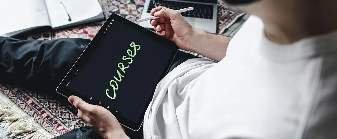 Adult learner writing "Courses" on a tablet while studying at home with a laptop and notebook