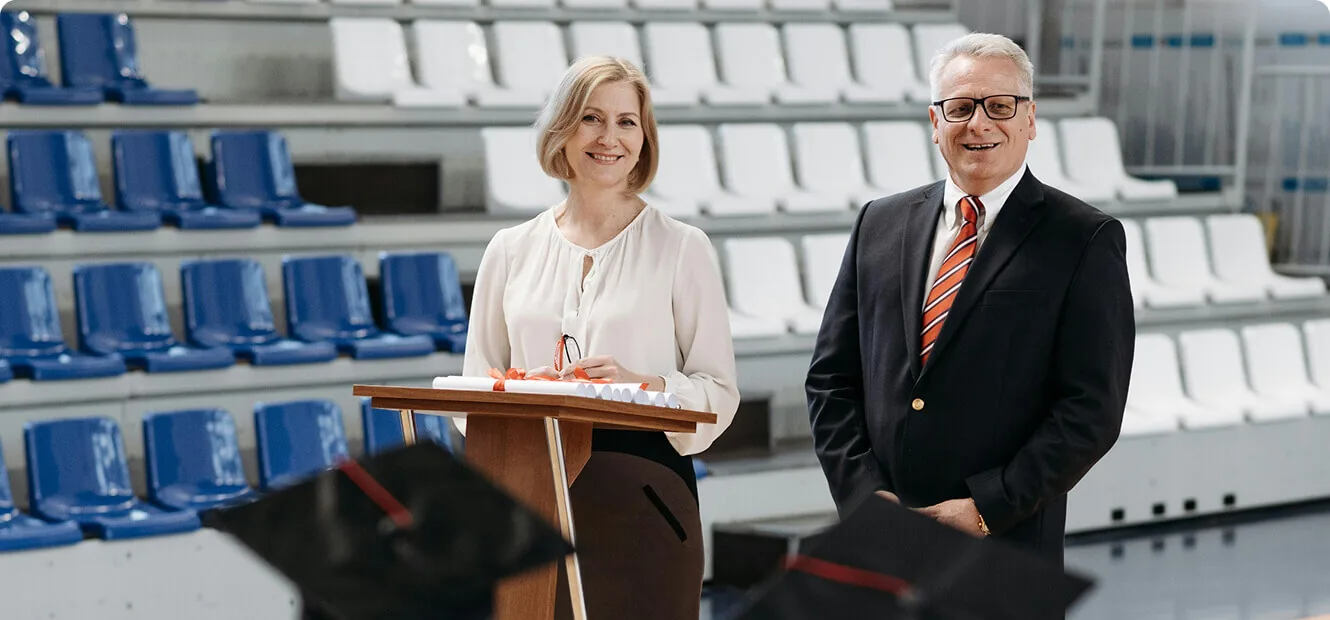 Two academic staff standing at a lectern with rolled diplomas at a graduation ceremony