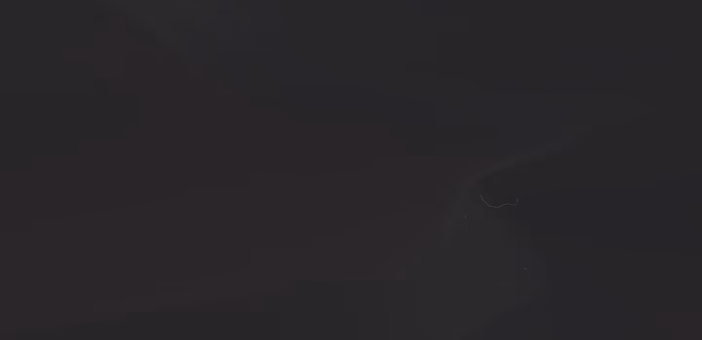 Close-up of a black domestic cat's face partially visible in low light against a dark background.