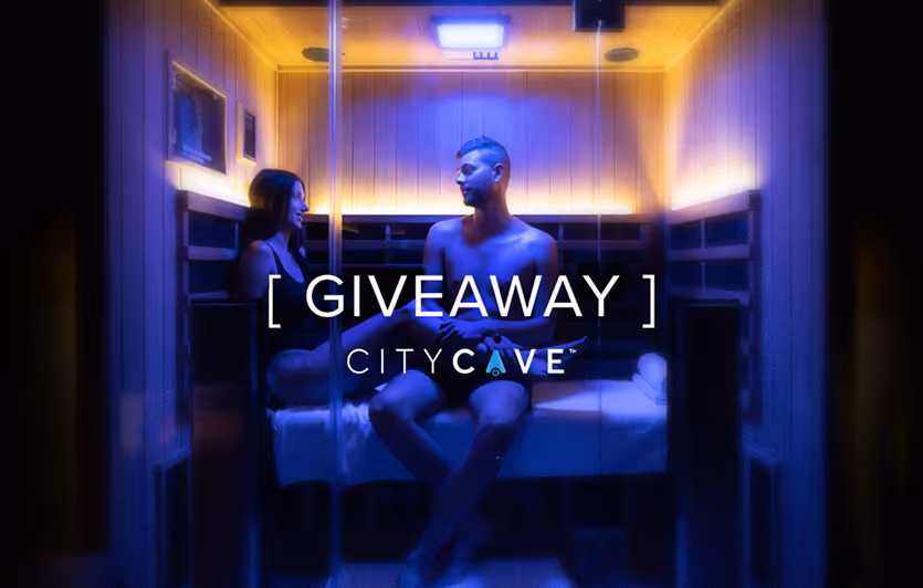 A man and woman sitting inside a small wooden sauna with soft yellow and blue lighting, with the words '[ GIVEAWAY ] CITYCAVE' overlayed.