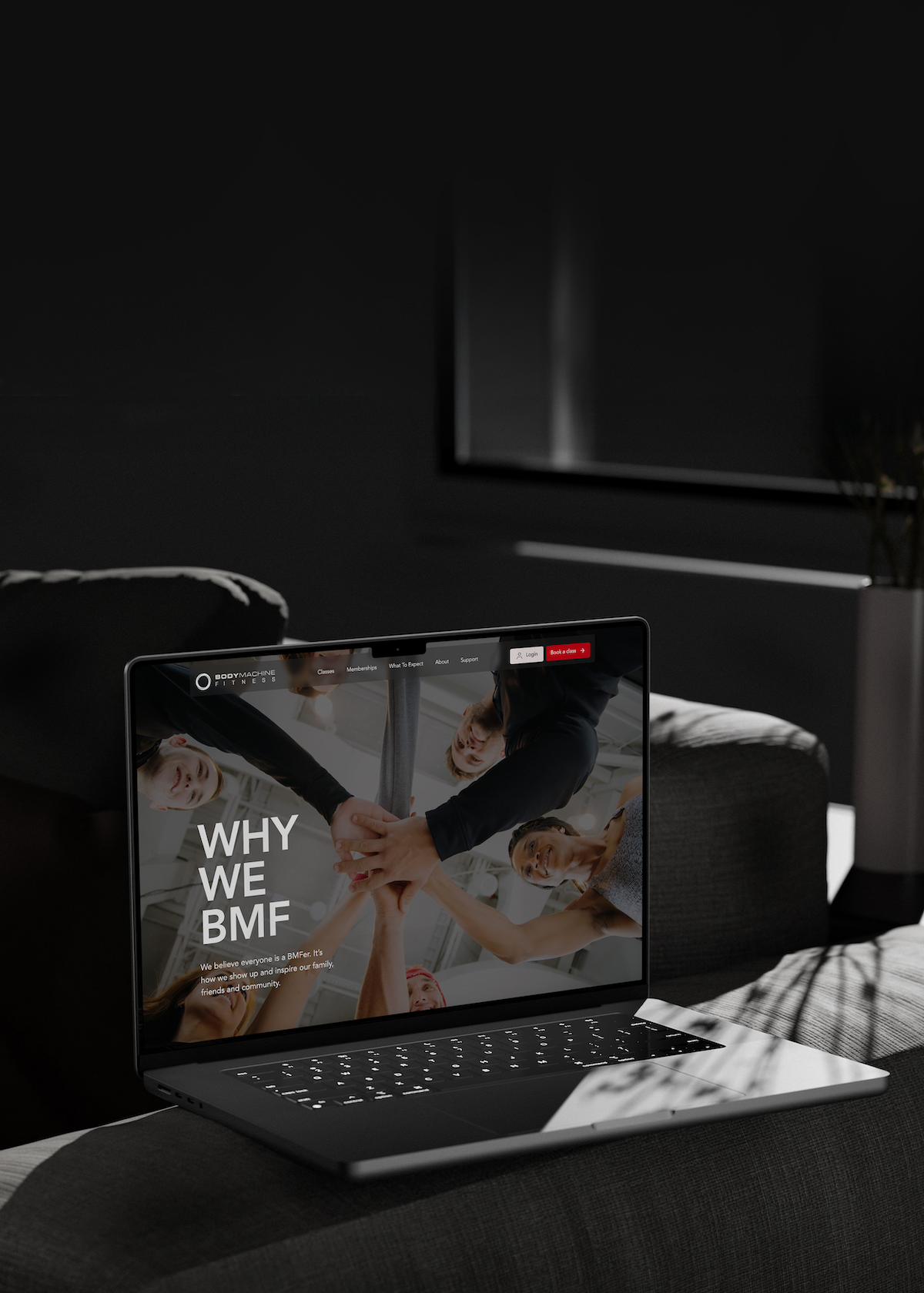 Laptop displaying a fitness website with the text 'WHY WE BMF' and an image of people joining hands in a team gesture.