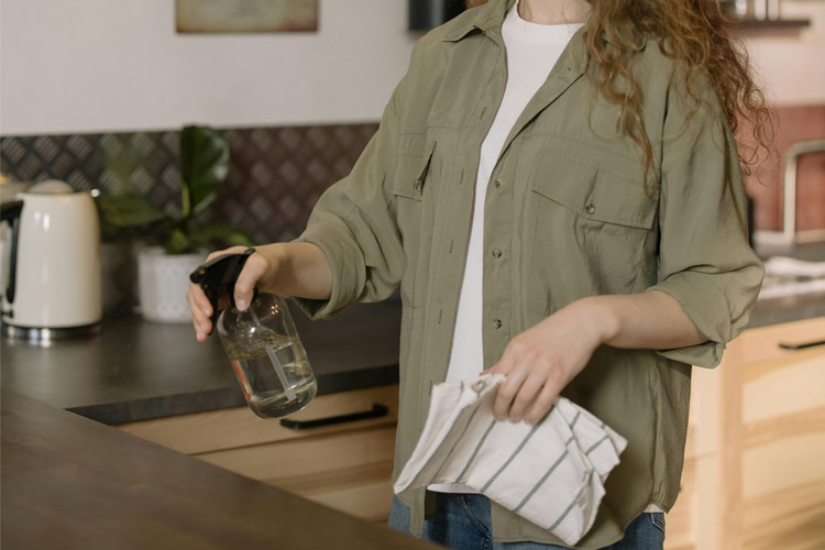 Person cleaning a kitchen counter with a spray bottle and cloth.