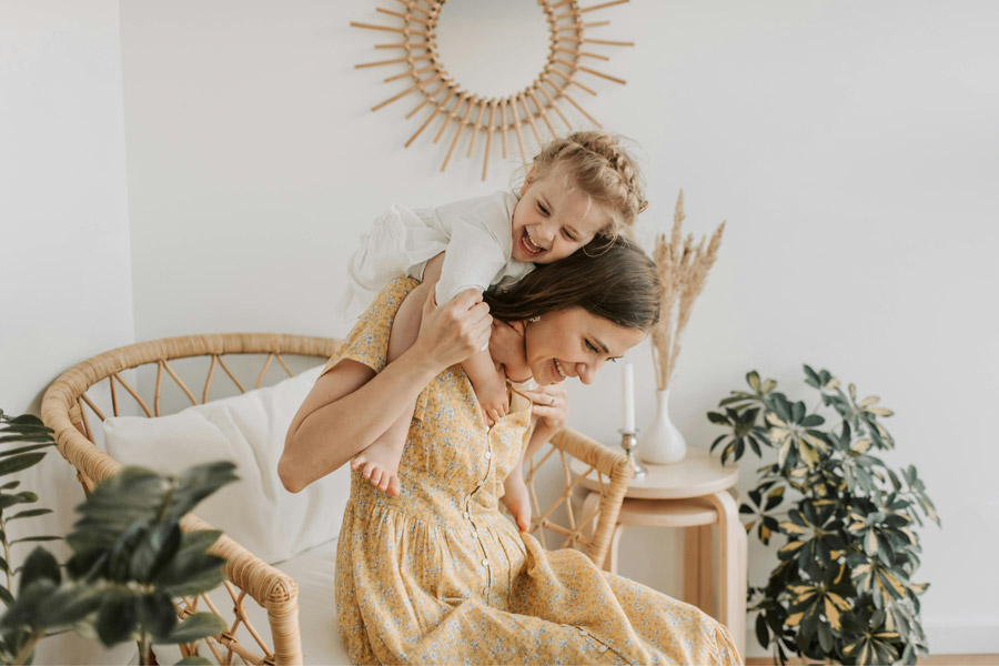 Mother and young child laughing together in a bright, cozy living space with natural décor and plants.