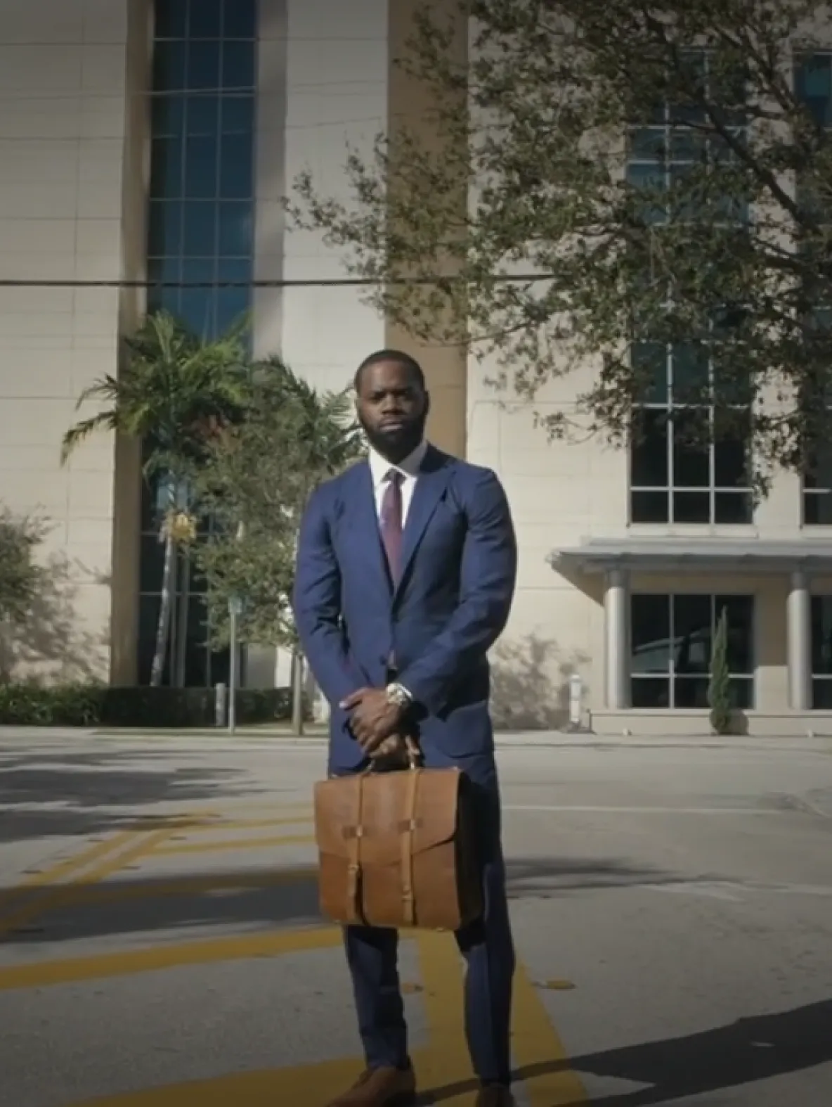 Man in a suit standing outside a large building with a briefcase.