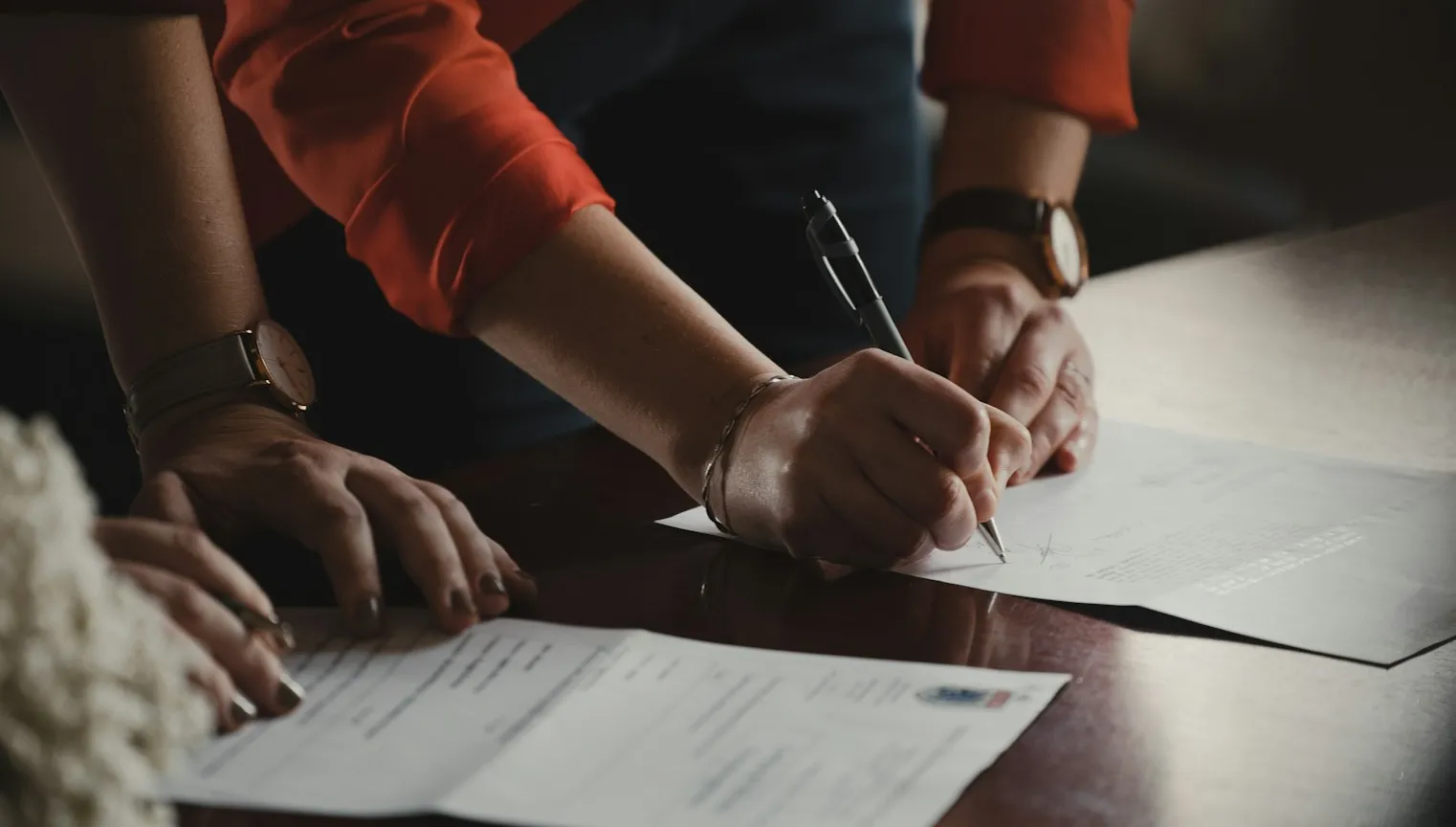 Hands signing documents on a desk.