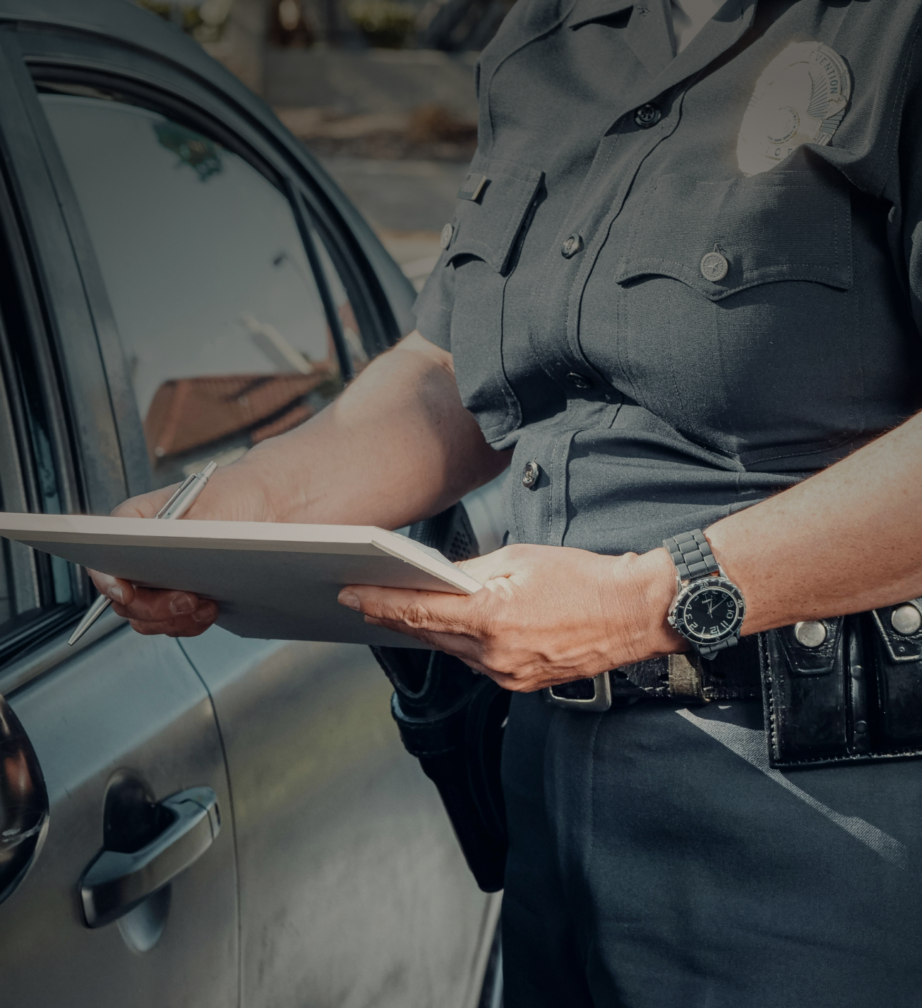 Police officer writing a report beside a car.